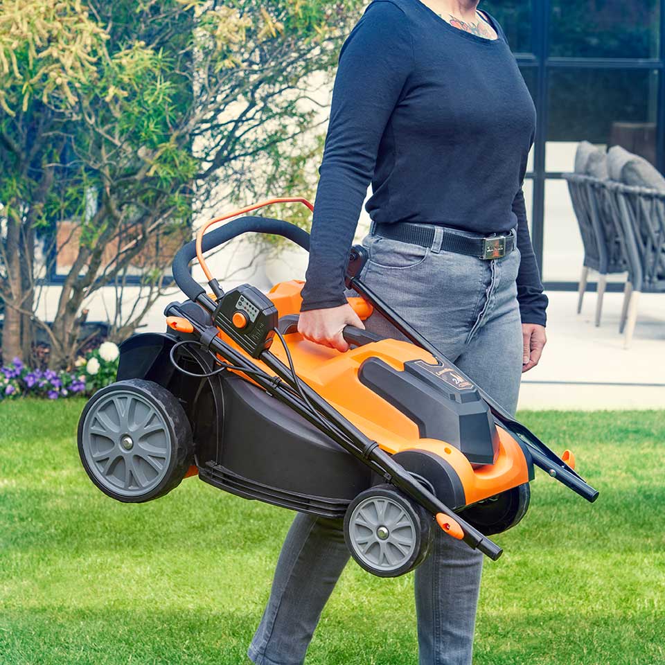 LawnMaster Akku-Rasenmäher (24 V, 37 cm) wird mit dem Griff durch den Garten getragen